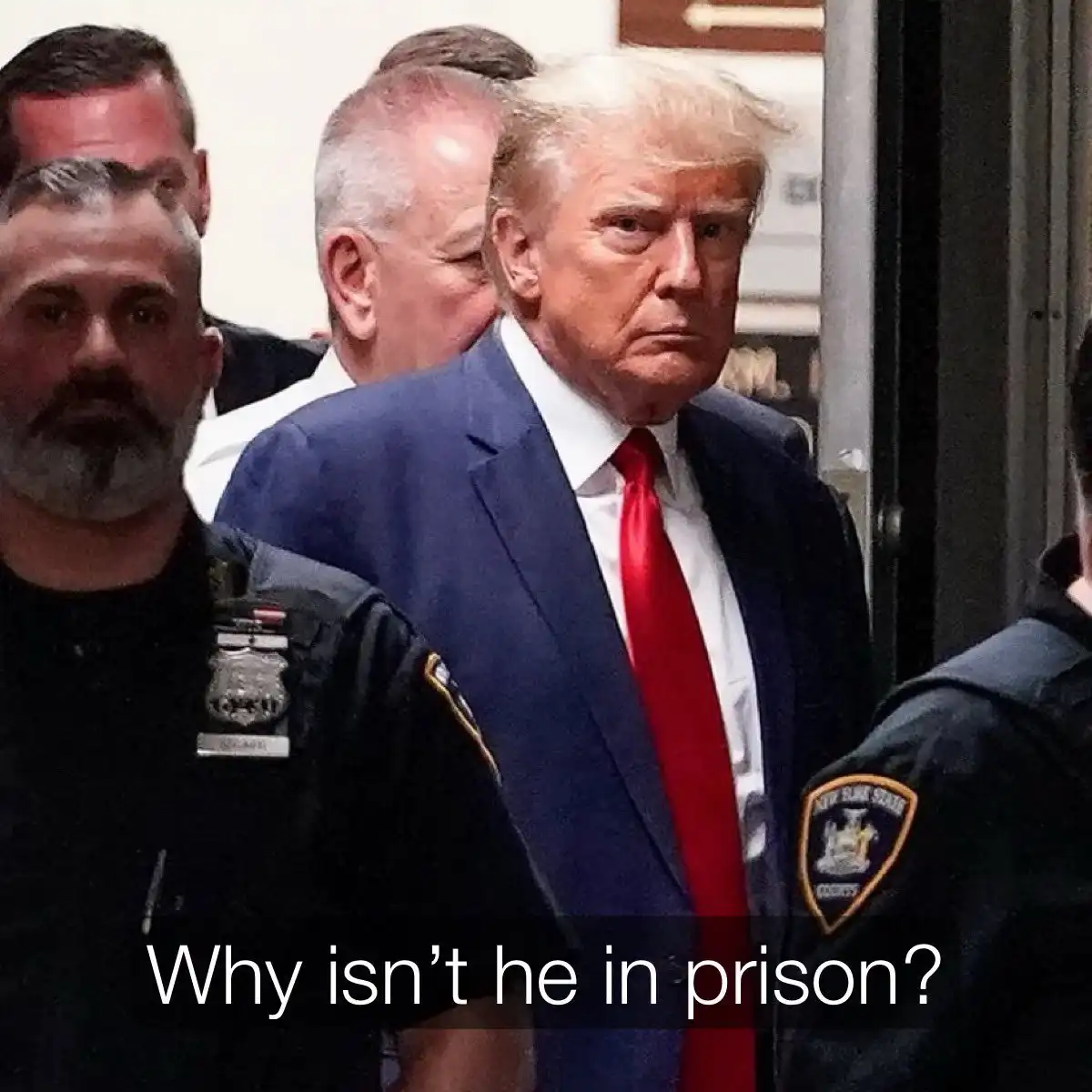 A photo shows Donald Trump in a blue suit and red tie, flanked by New York State police officers, looking serious as he…