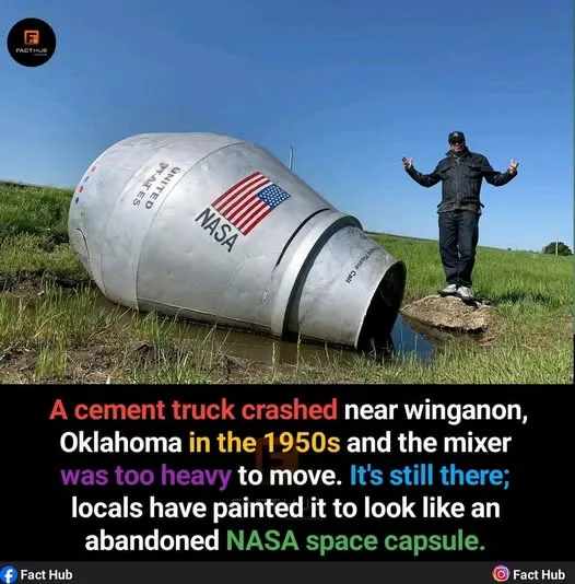 A large, silver, cylindrical object painted with 'UNITED STATES' and a NASA logo, resembling a space capsule, lies tilted in…
