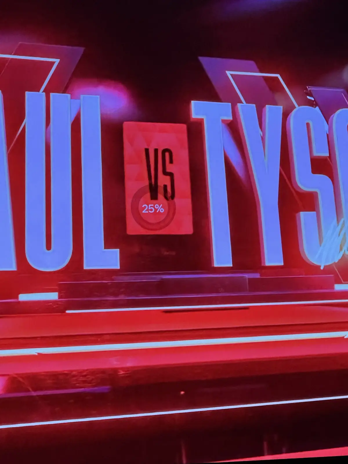 A close-up of a red and blue TV screen graphic showing the text 'VS' with '25%' below it, set between large stylized letters…