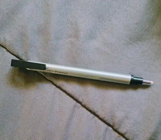A silver pen with a black cap and tip lies diagonally on a gray fabric surface. The pen's body has visible text including…