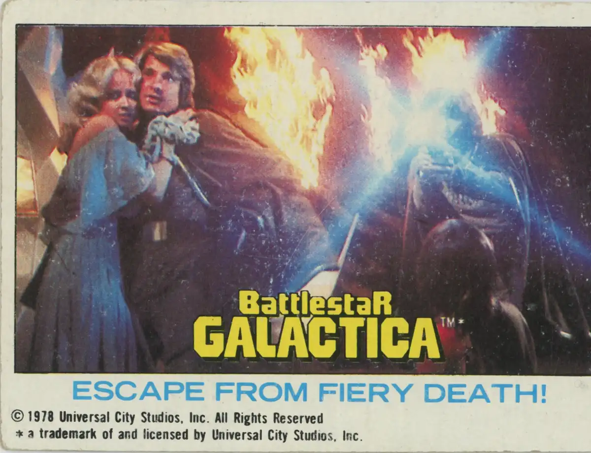 A vintage 1978 Battlestar Galactica trading card depicts a dramatic scene with two characters in a fiery explosion, one…