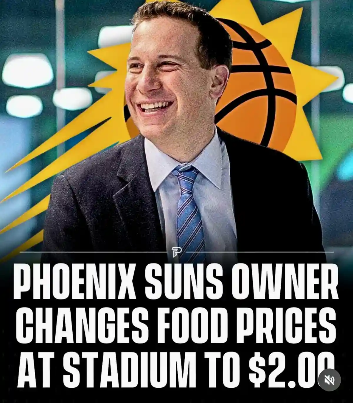 A man in a suit and tie smiles broadly against a background featuring the Phoenix Suns basketball team logo. Large white…