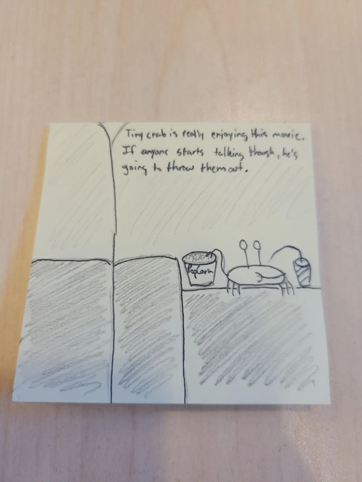 A hand-drawn comic on a sticky note shows a tiny crab sitting in a theater with a popcorn bucket and drink, enjoying a…