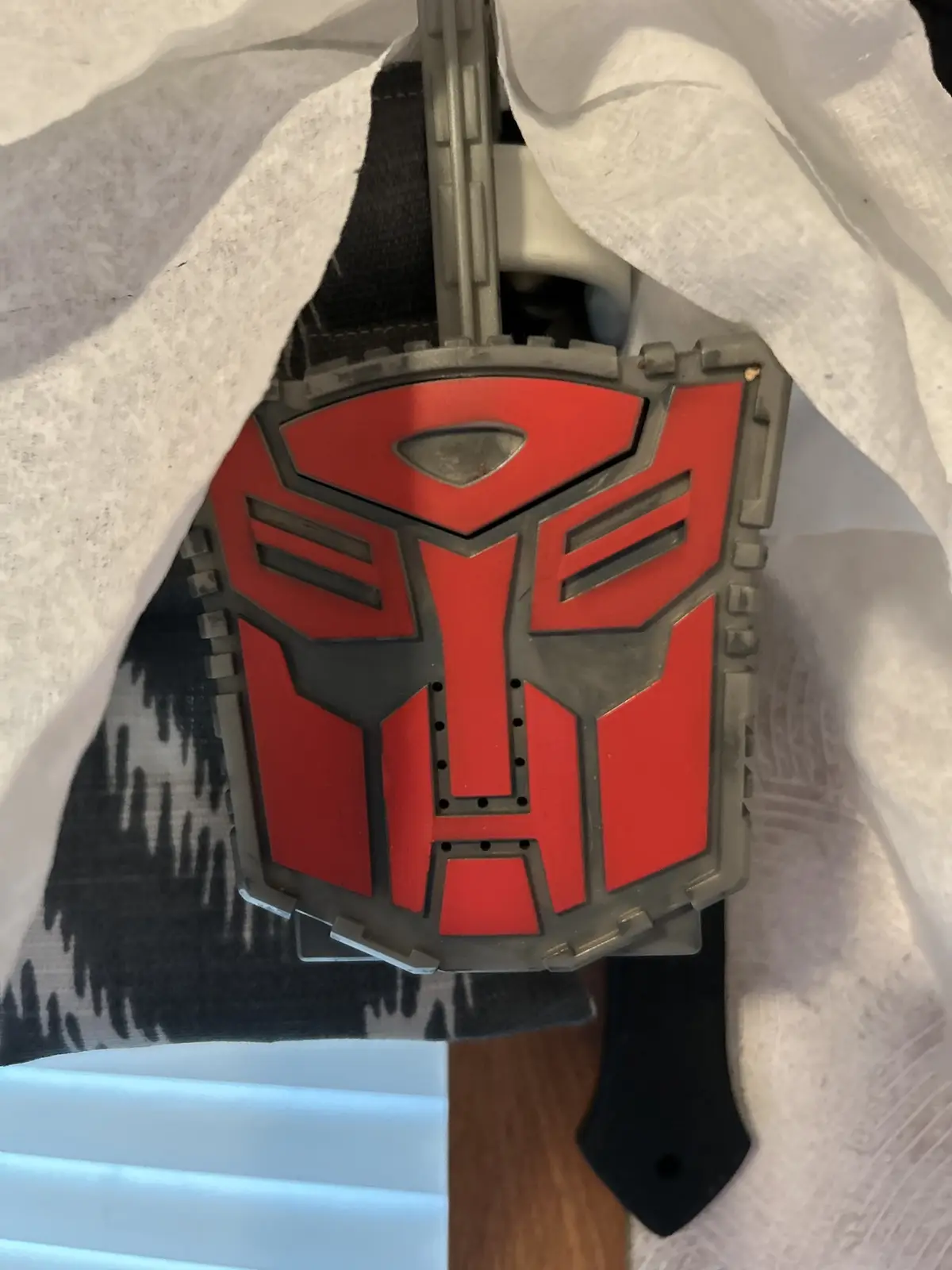 A red and grey Autobot logo from Transformers is partially covered by white paper towels, revealing only its central…