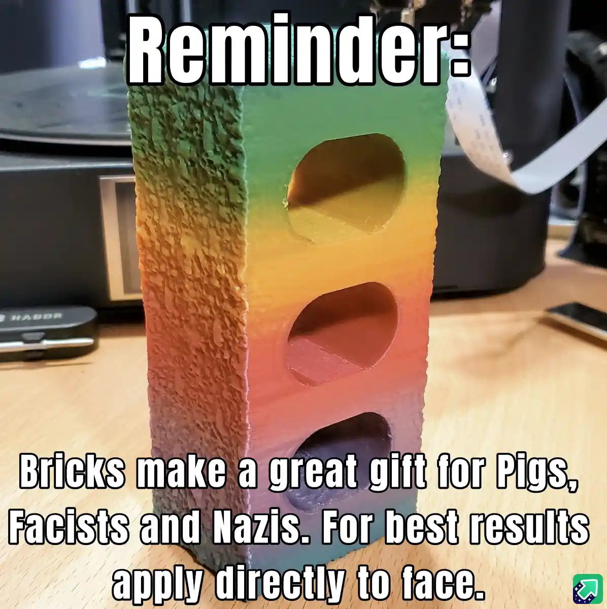 A 3D-printed, rainbow-colored traffic light-shaped object with three circular holes sits on a wooden desk. The overlaid text…