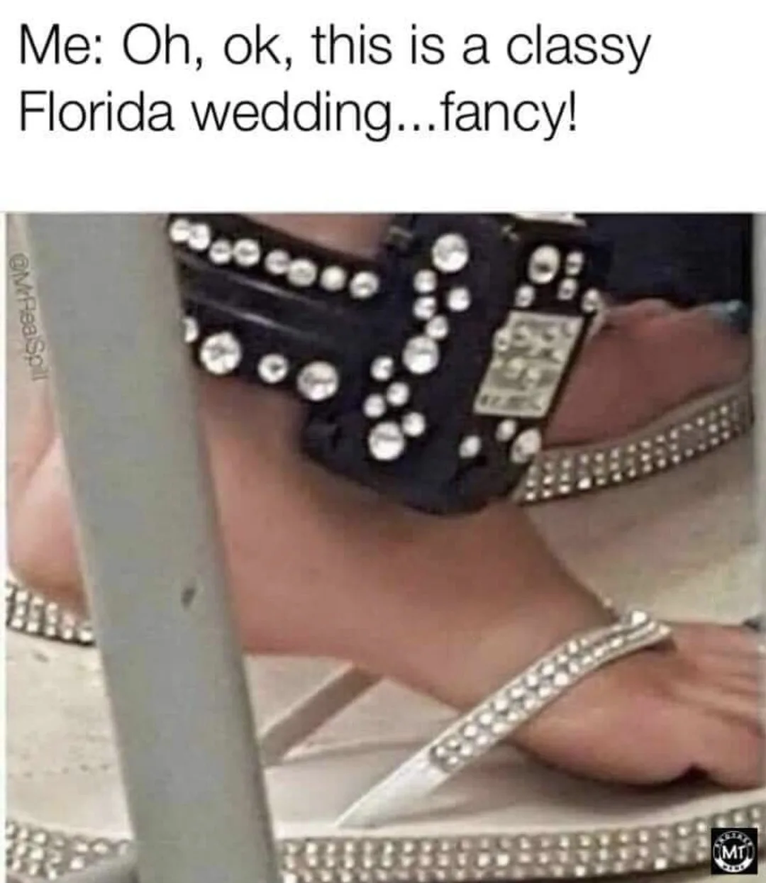 A close-up photo shows a person's foot wearing a white flip-flop heavily adorned with rhinestones, with a black, similarly…