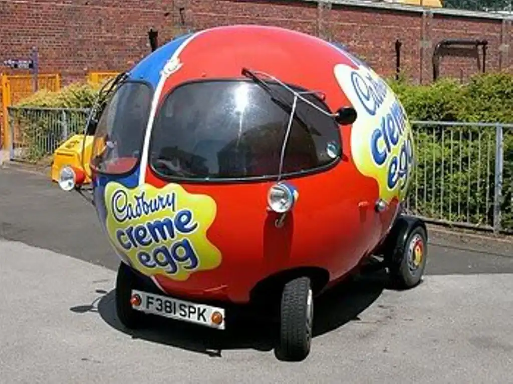 A small, egg-shaped vehicle painted to resemble a Cadbury Creme Egg, featuring the brand's logo and colors, parked on a…