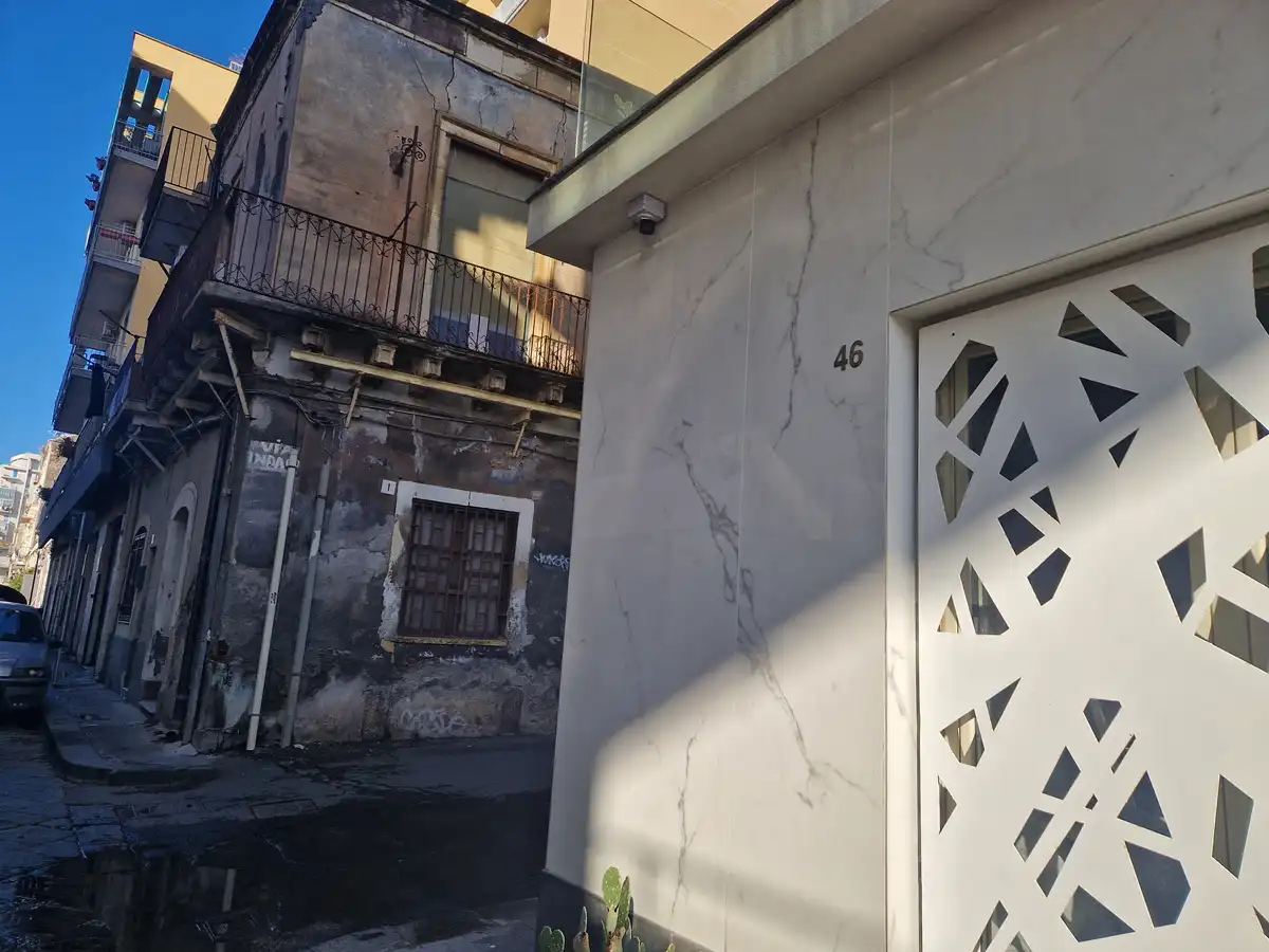 A street view shows a stark contrast between a modern, pristine white marble building with the number 46 and a dilapidated…