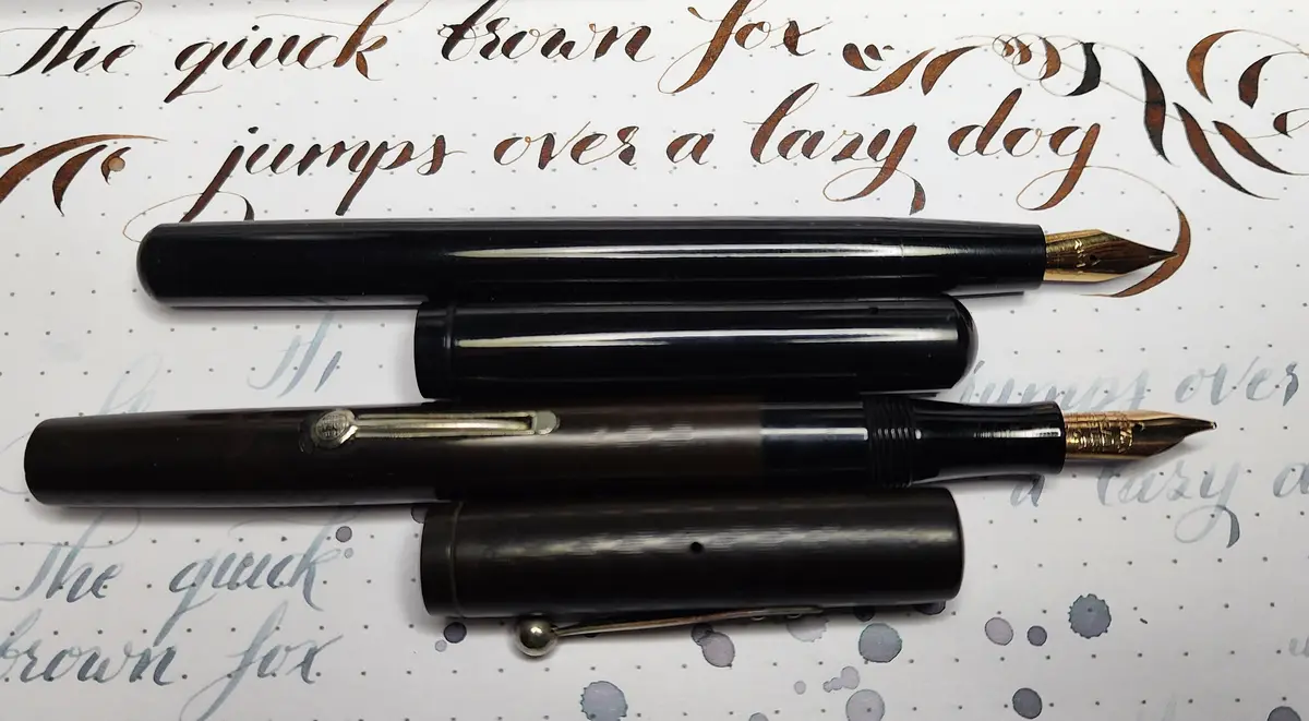 Two fountain pens with their caps off are laid horizontally on a sheet of paper with the pangram 'the quick brown fox jumps…