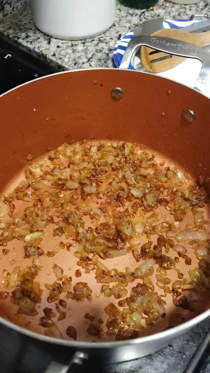 A close-up photo shows a copper-colored frying pan on a stovetop, filled with caramelized onions that are golden brown and…