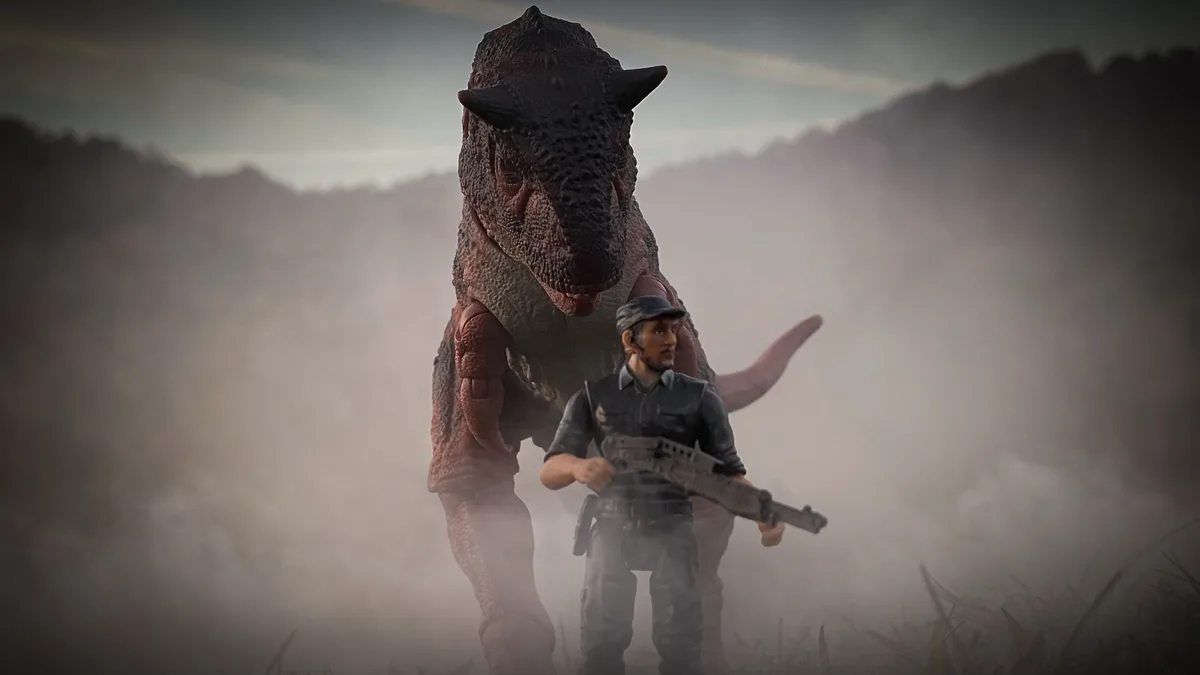 A toy action figure of a man holding a rifle stands in front of a large toy dinosaur, both positioned in a misty…
