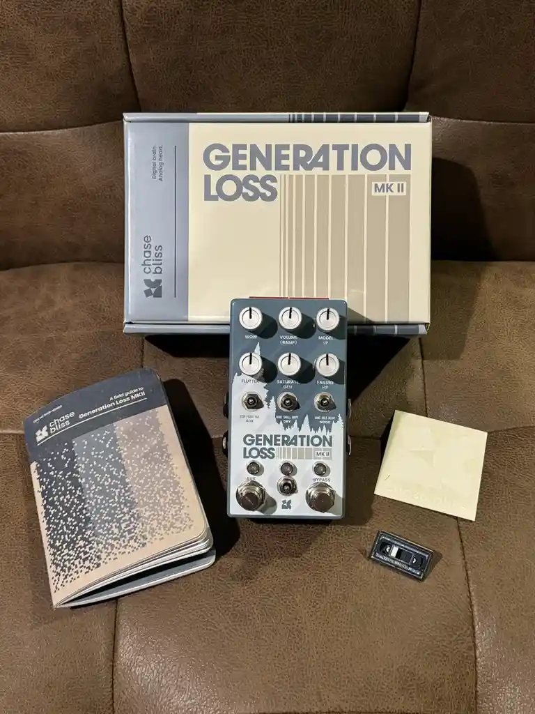 A Chase Bliss 'Generation Loss MKII' guitar effects pedal sits on a brown leather couch next to its box, a field guide…