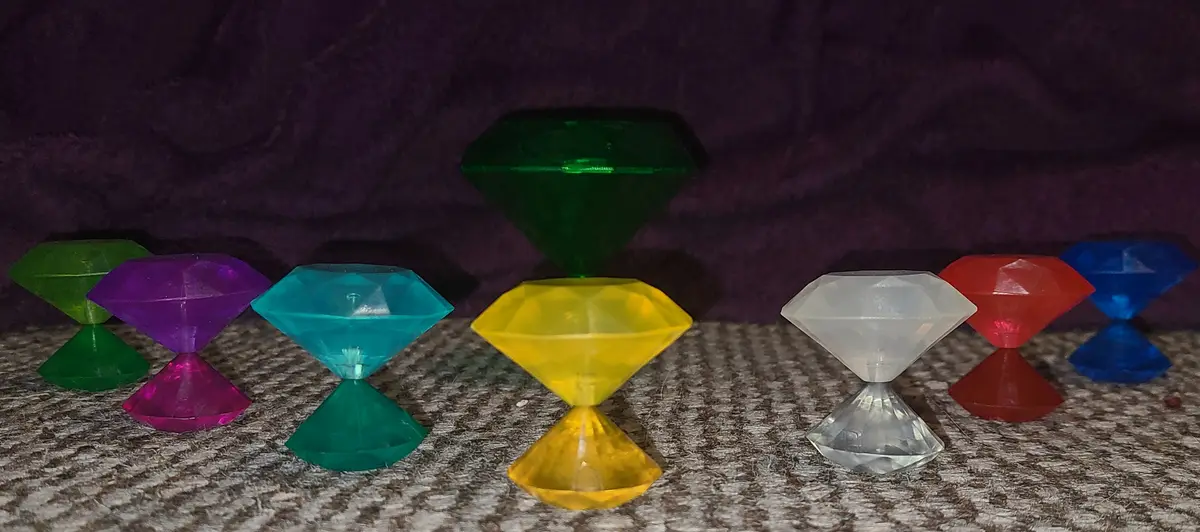 A row of colorful, plastic, diamond-shaped objects with faceted tops and bases sit on a textured carpet against a dark…