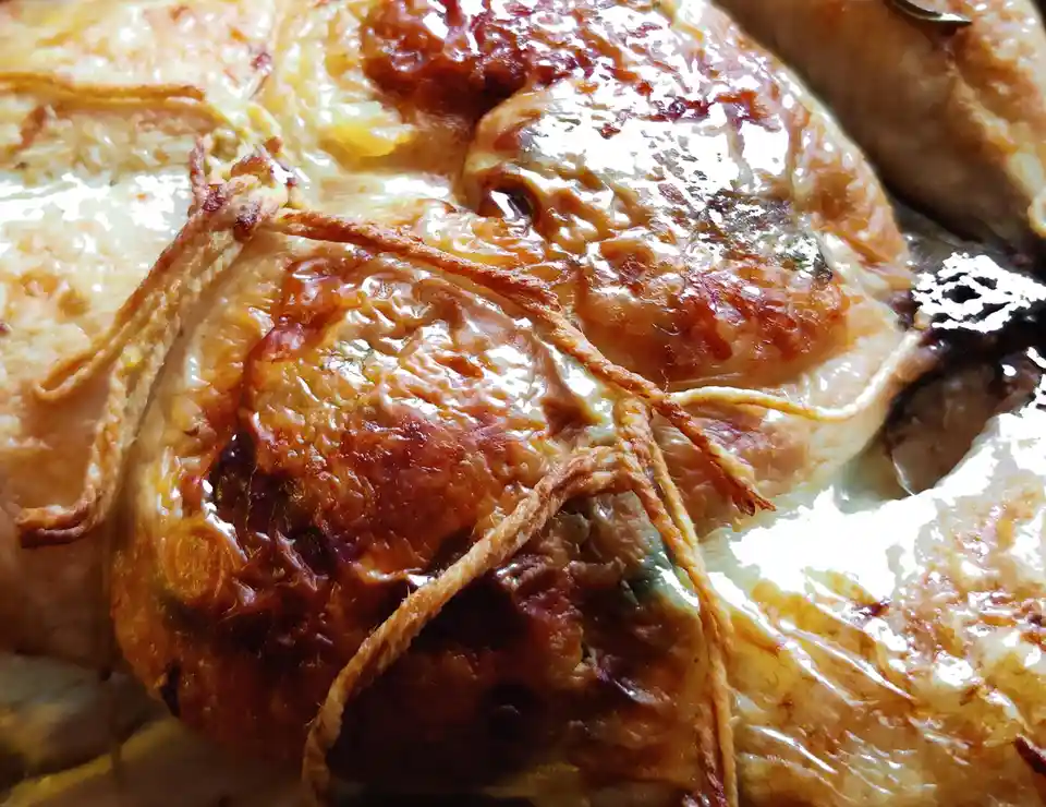 A close-up photo of roasted chicken pieces with golden-brown, glistening skin and crispy fried onion strings tied around…