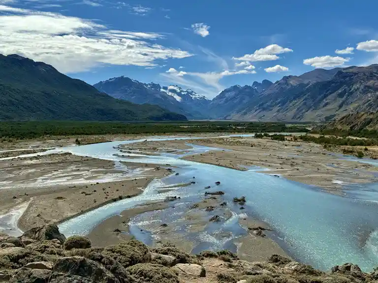 A scenic landscape photo shows a winding, turquoise river flowing through a wide valley with sandy banks, surrounded by lush…