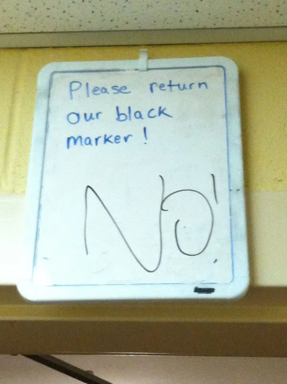 A small whiteboard with blue handwriting reads 'Please return our black marker!' and below it, 'No!' is written in large…