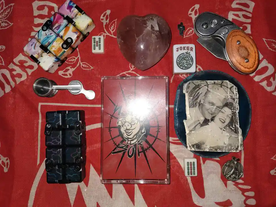 An overhead shot displays a collection of eclectic items arranged on a red fabric with white text and patterns, including a…