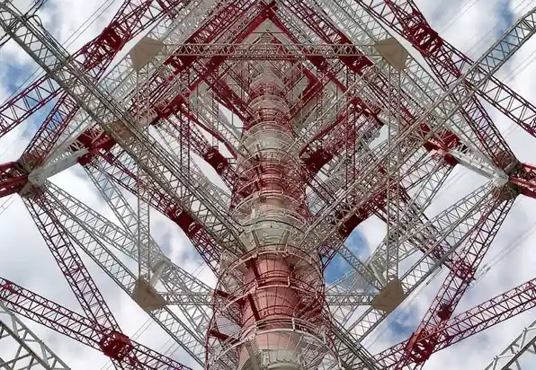 A low-angle photograph looking up at the red and white lattice structure of the Tokyo Tower against a partly cloudy sky. The…