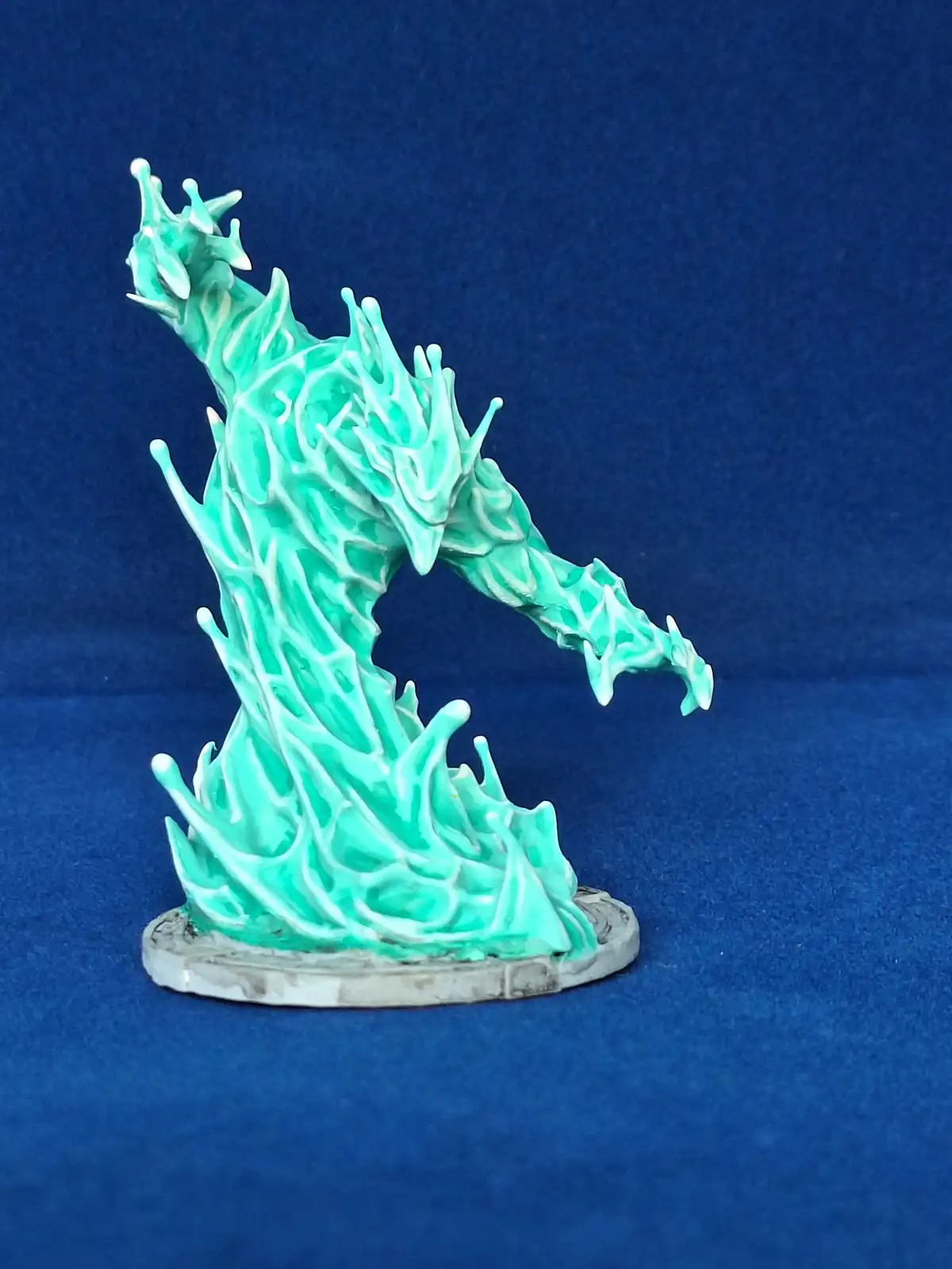 A teal-painted miniature figurine shaped like a stylized, flame-like dragon with a dynamic, arched pose, standing on a grey…