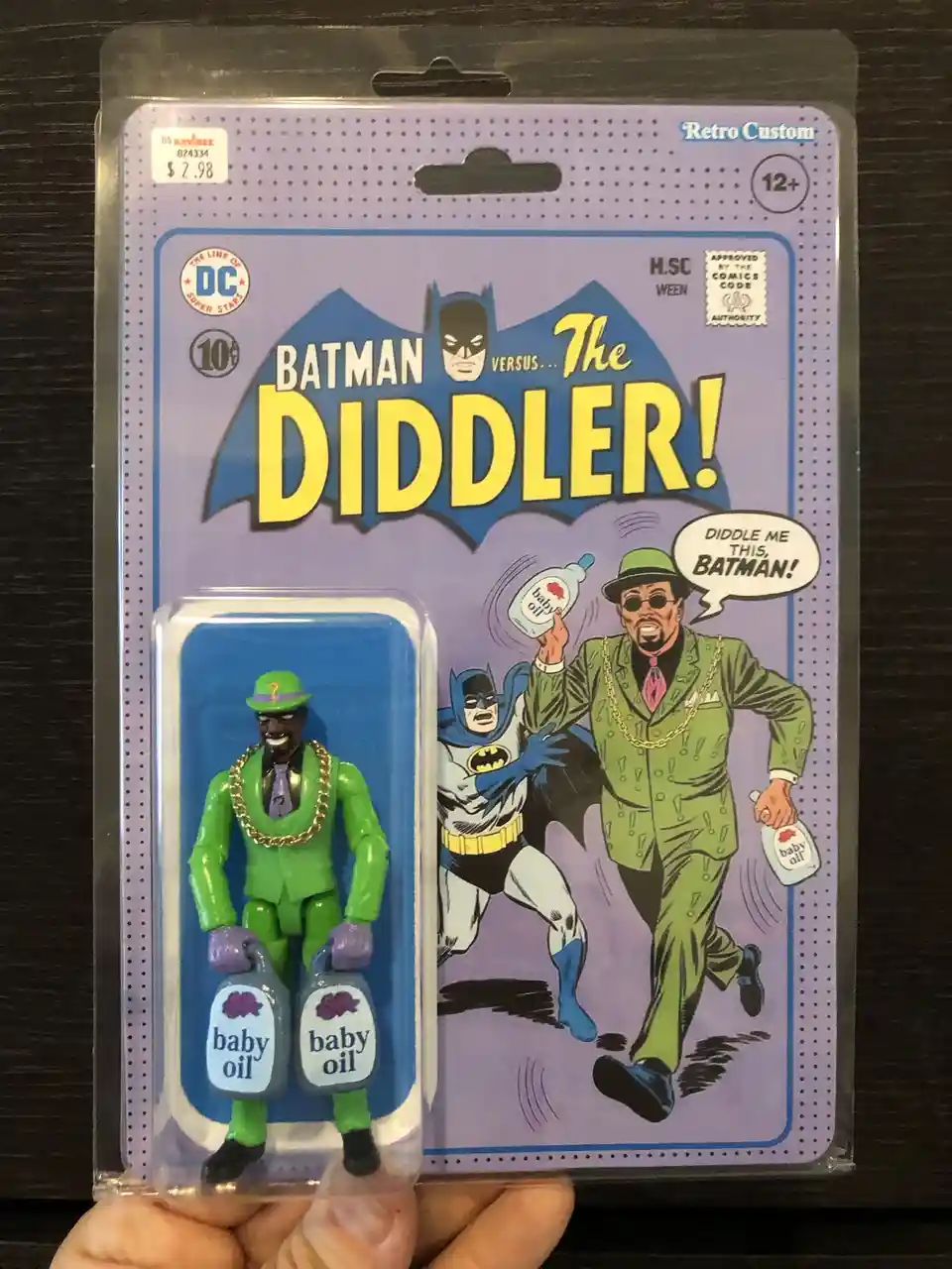 A person holds a retro-style Batman action figure package featuring The Diddler. The packaging mimics a vintage comic book…
