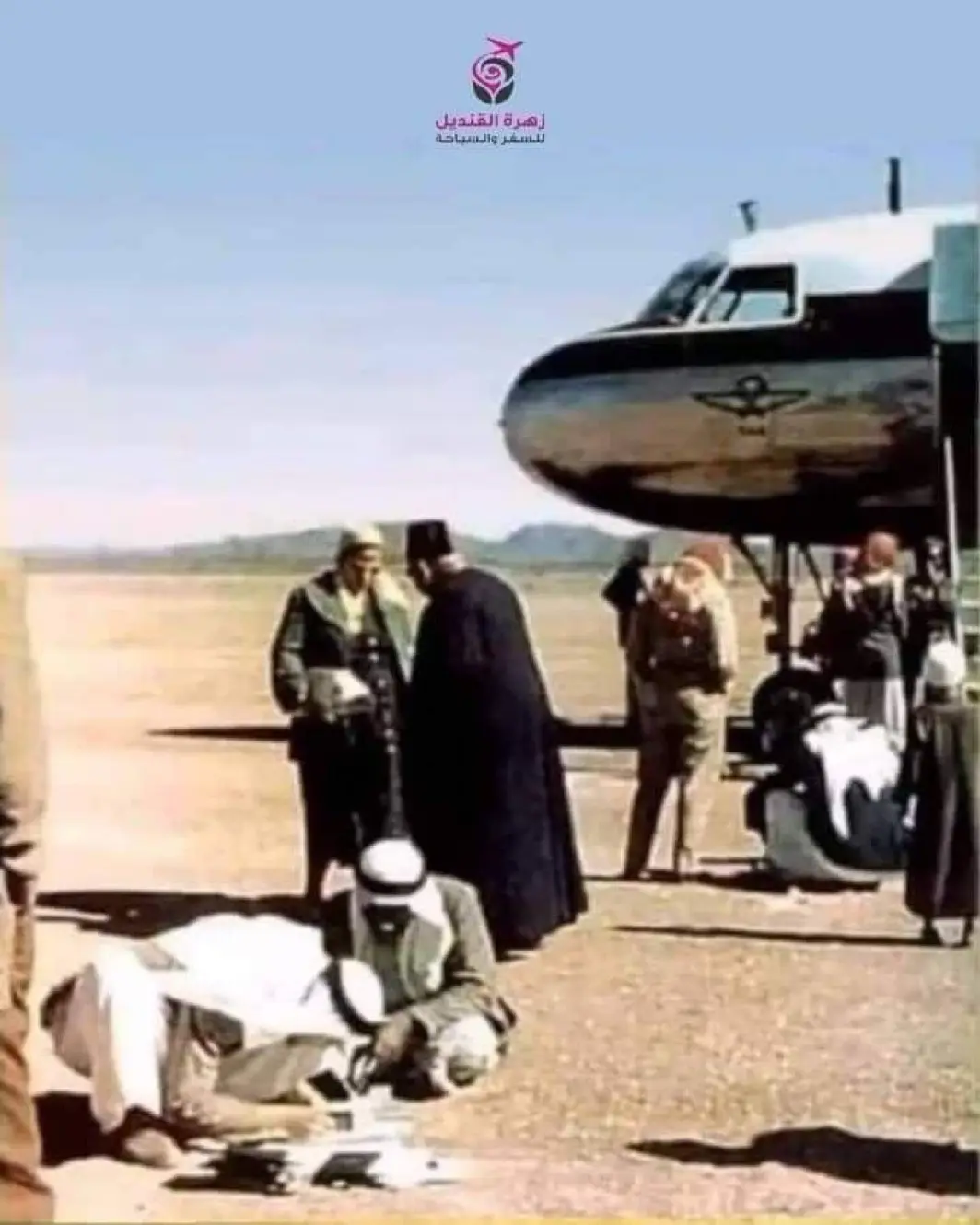 A vintage photo shows several men in traditional Middle Eastern attire on a dusty airfield beside an old airplane. One man…