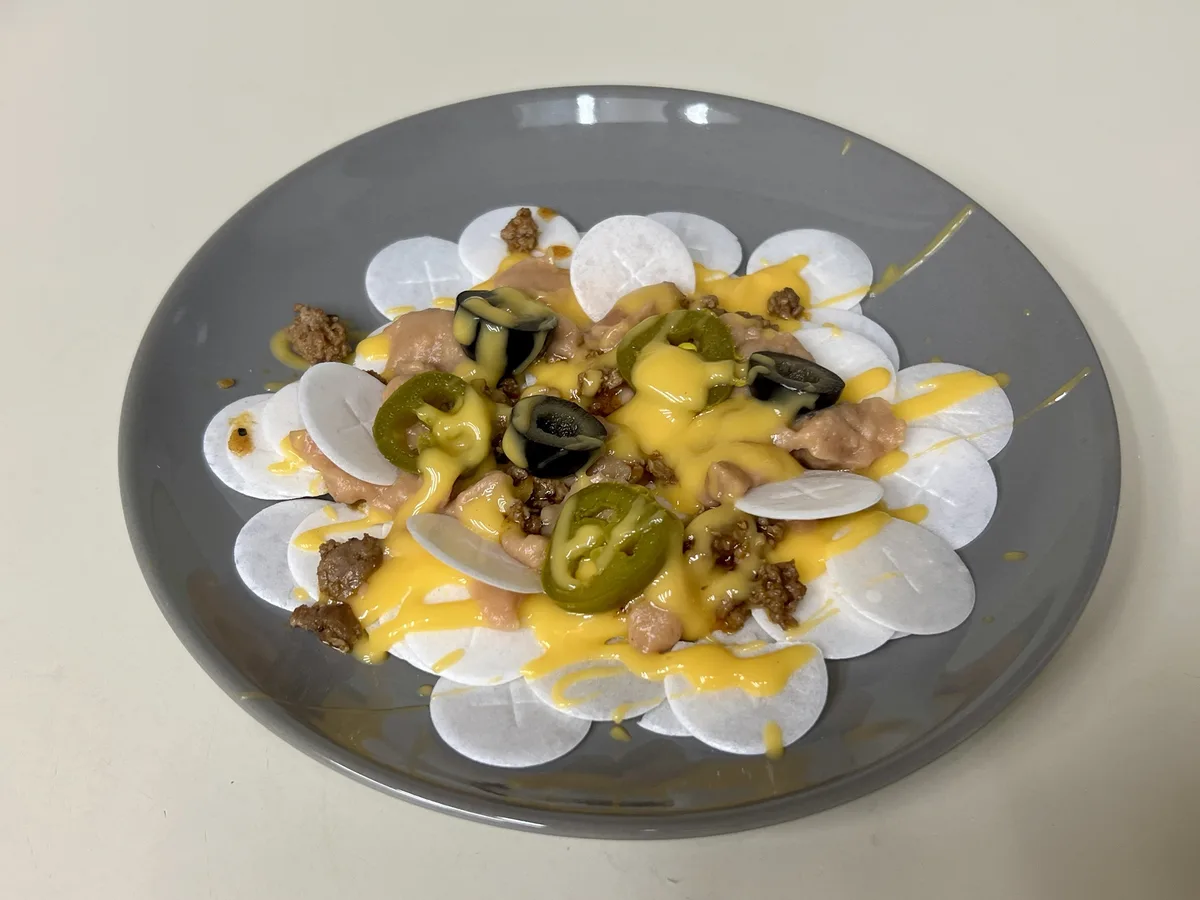 A gray plate holds a dish that visually resembles nachos, but the base consists of white, round, textured toilet paper discs…