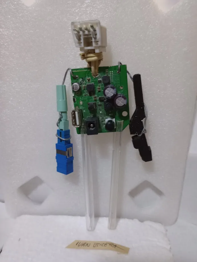 A green circuit board is assembled into a humanoid figure using clear plastic rods for legs, a white connector as a head…