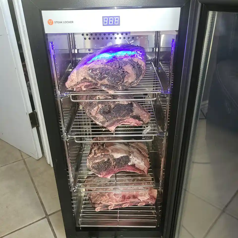 A black 'Steak Locker' appliance with a digital display showing '888' contains four large raw beef cuts on metal racks…