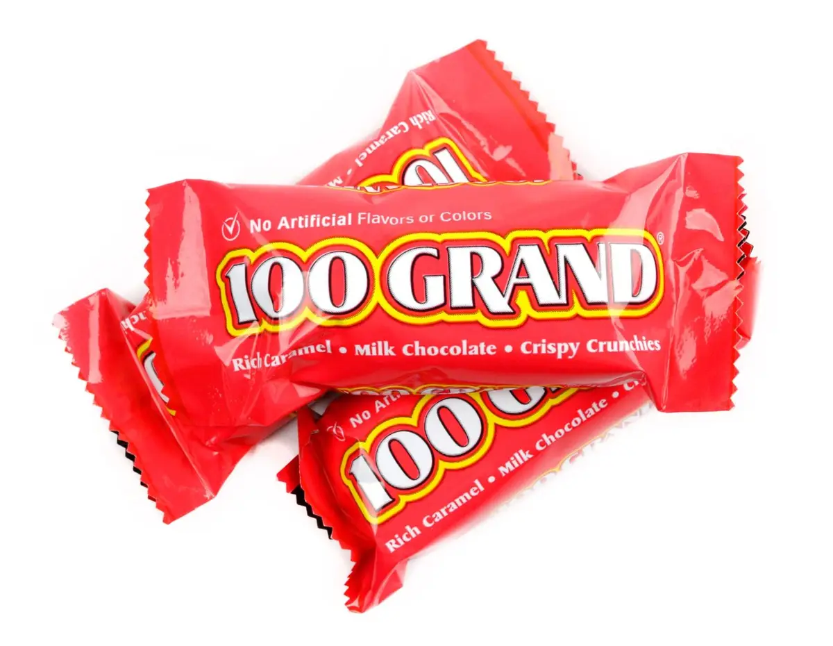 Several red-wrapped 100 Grand candy bars are piled together against a white background. The packaging prominently displays…