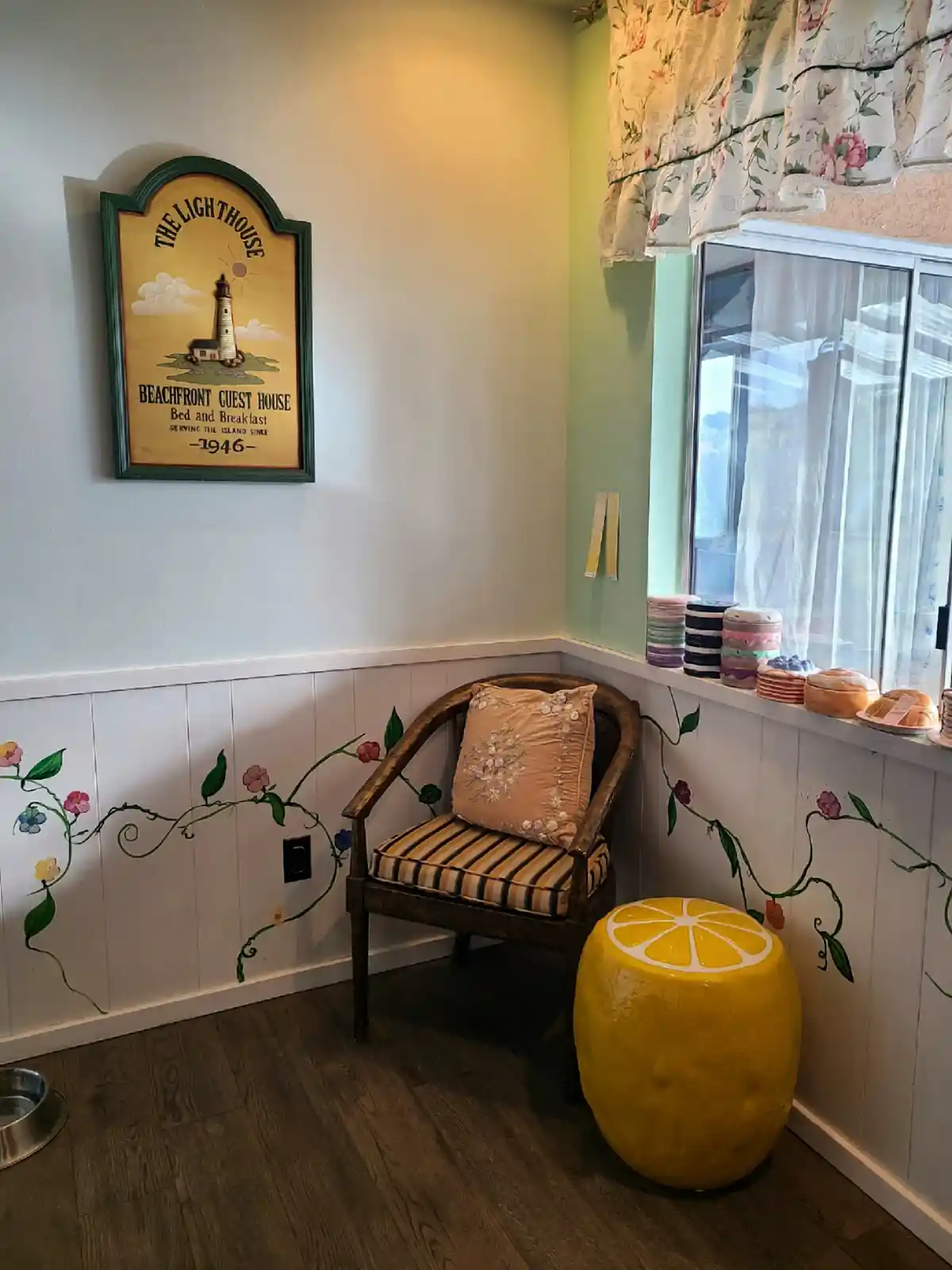 A cozy corner of a room with a wooden chair and a large yellow lemon-shaped ottoman, next to a window with floral curtains…