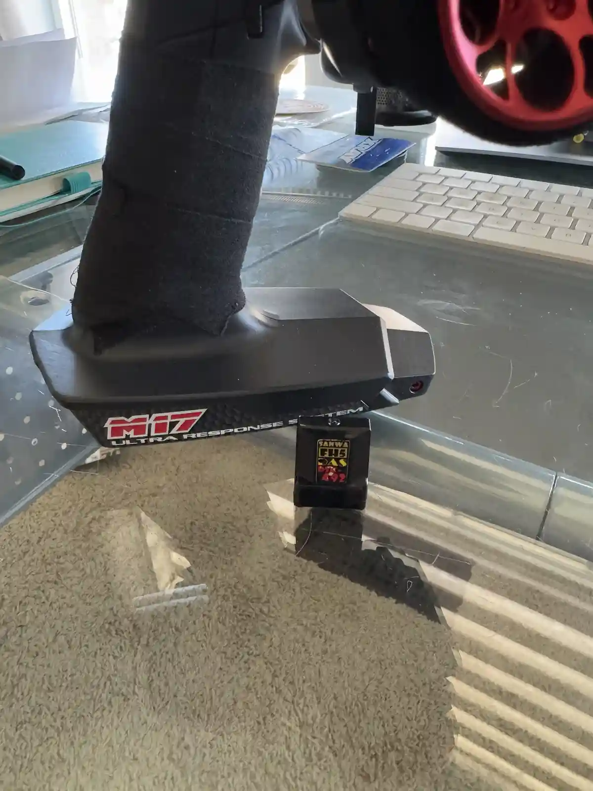 A person's foot, wrapped in black fabric like a cast, is resting on the throttle pedal of a radio-controlled car. The car's…