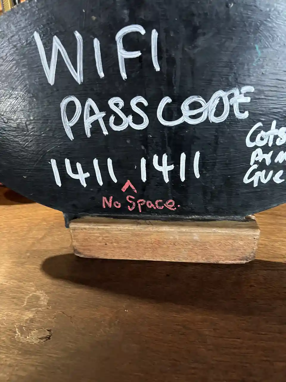 A close-up of a black chalkboard sign on a wooden stand, written in white chalk, displays 'WIFI PASSCODE 1411 1411' with a…