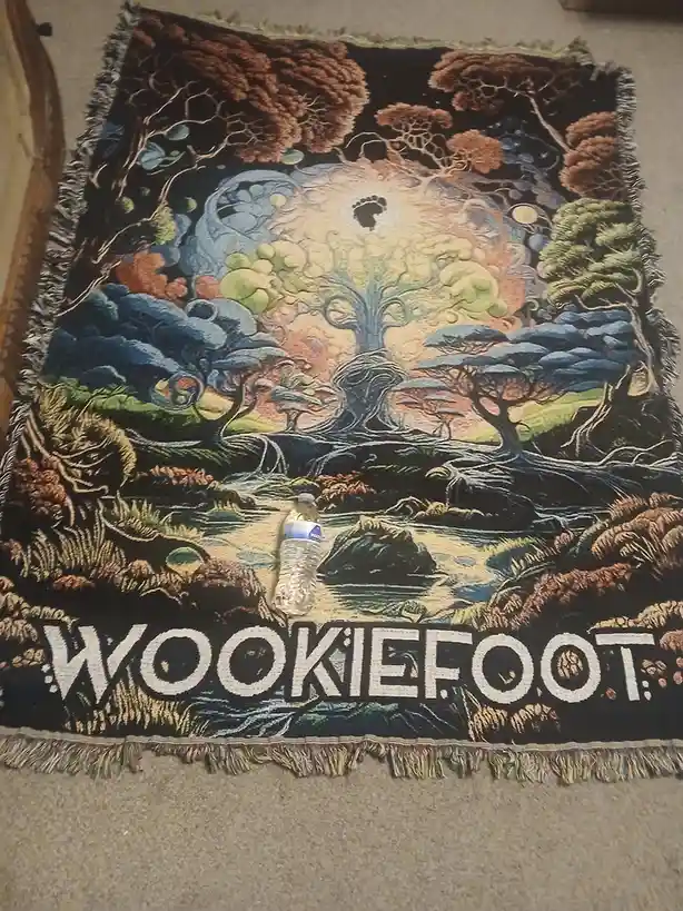 A woven tapestry depicting a mystical forest scene with a central tree, swirling clouds, and a glowing moon with a paw…