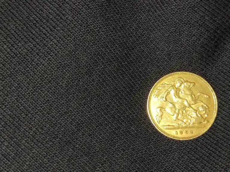 A gold coin dated 1992, featuring a relief of St. George on horseback slaying a dragon, rests on a dark gray textured…