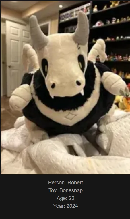 A large, white and black plush toy resembling a horned, dragon-like creature with a black collar and small horns, sits on a…