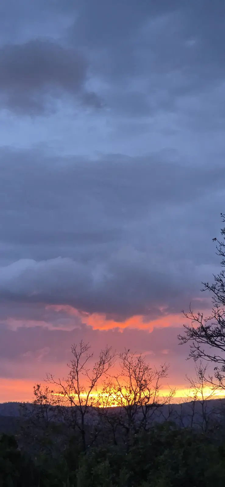 A scenic photograph of a dramatic sunset or sunrise with orange and pink hues glowing beneath dark, layered clouds…