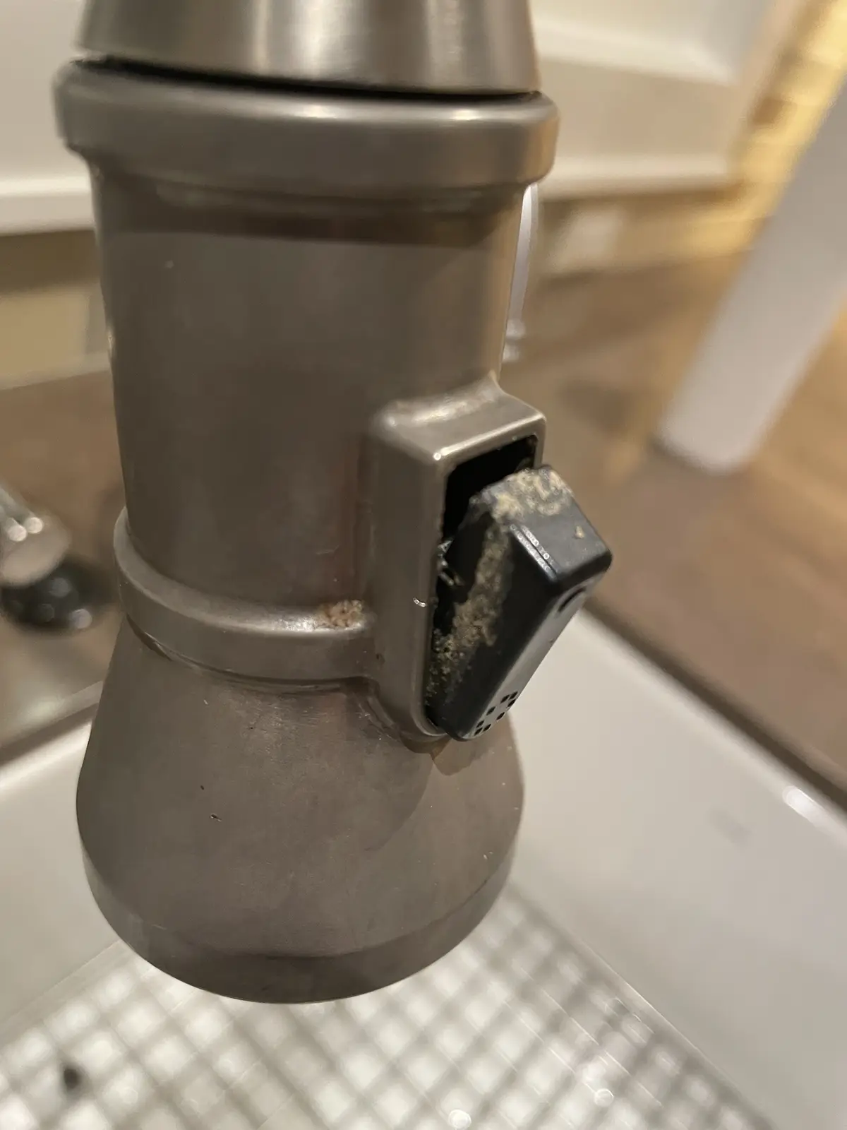 A close-up photo shows a stainless steel coffee maker with a black lever handle heavily caked in dark coffee grounds and…