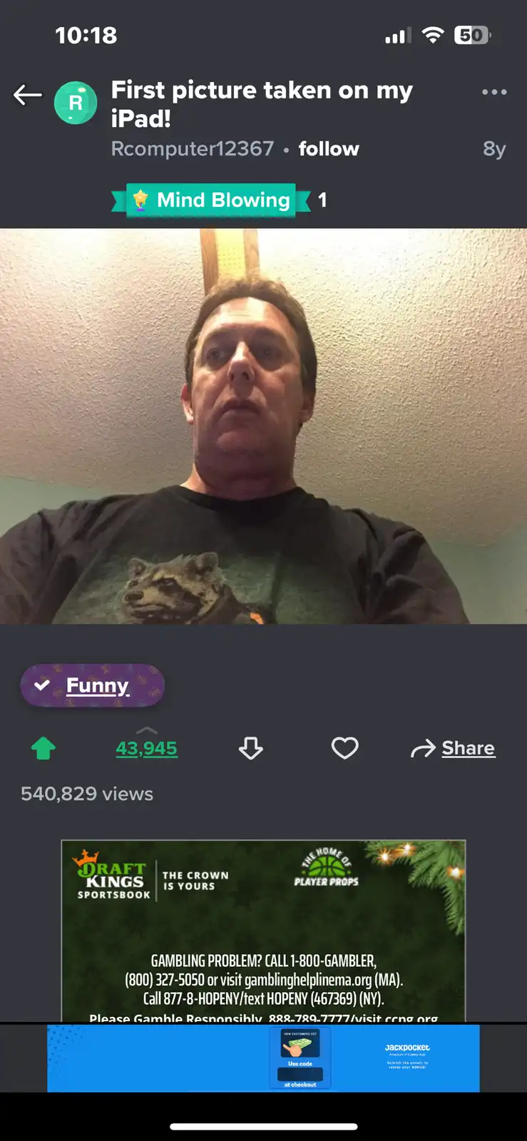 A screenshot of a social media post showing a man in a dark t-shirt with a raccoon graphic looking upward with a confused or…