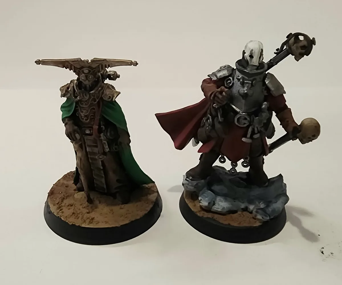 Two painted fantasy miniatures stand side-by-side on circular bases against a plain white background. The figure on the left…