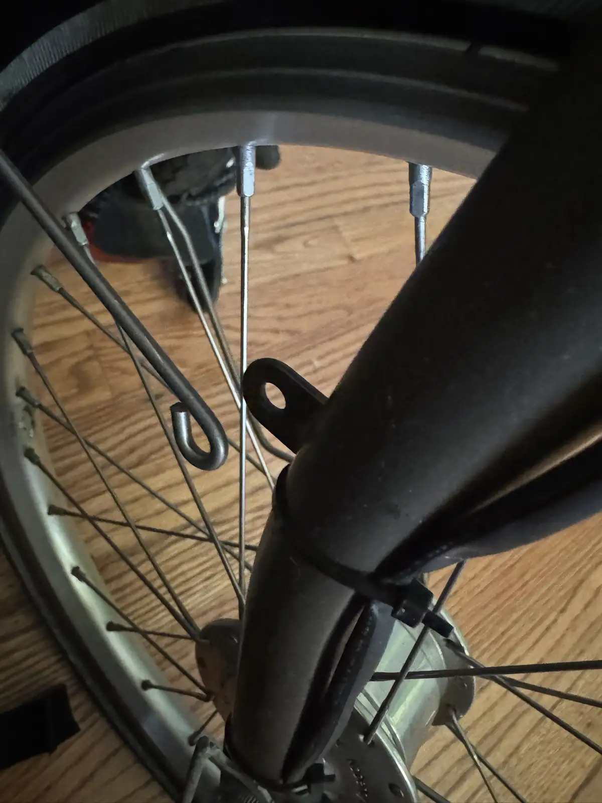 A close-up photo of a bicycle wheel's front fork and spokes, with a small metal hook attached to one of the spokes, resting…