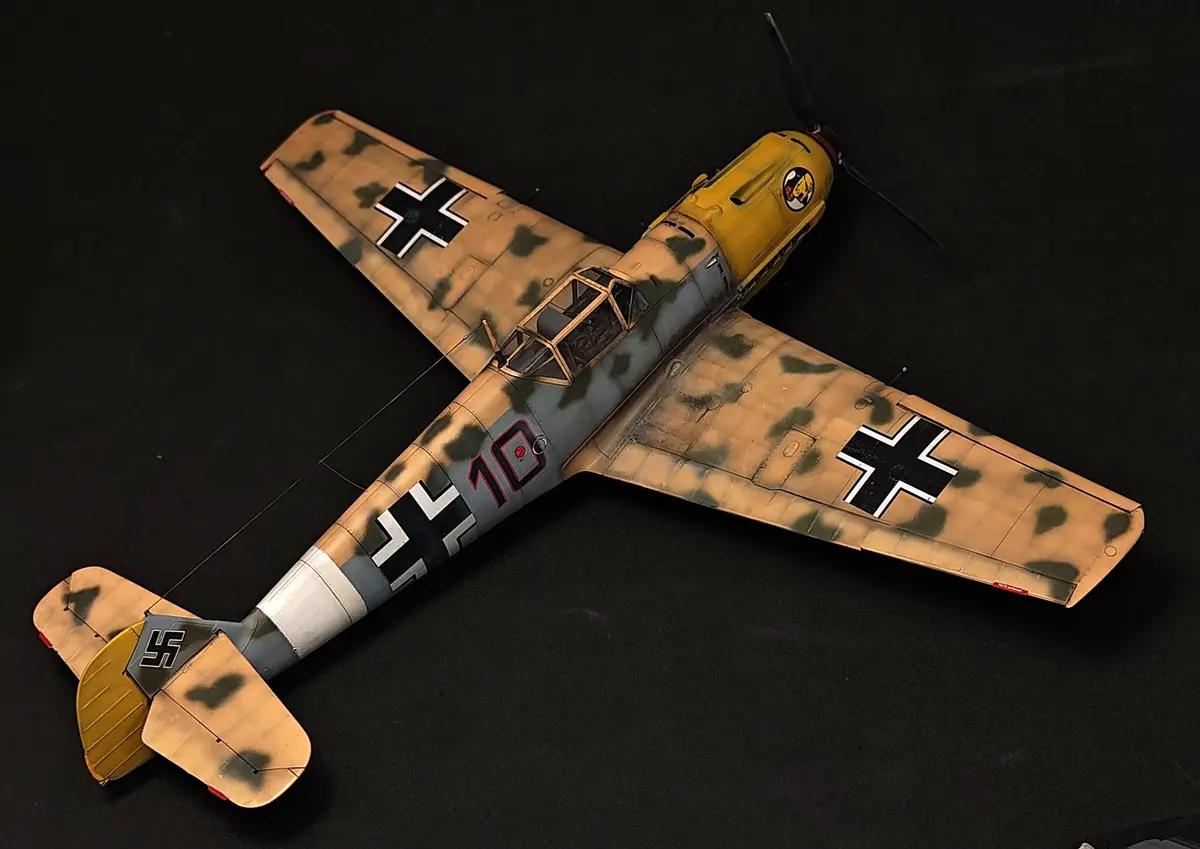 A detailed scale model of a German World War II fighter plane, likely a Messerschmitt Bf 109, is displayed against a black…