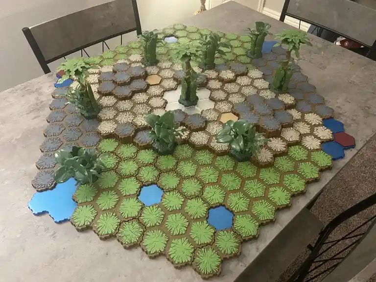 A tabletop game board made of interlocking hexagonal tiles in green, blue, and gray, arranged to form a jungle landscape…