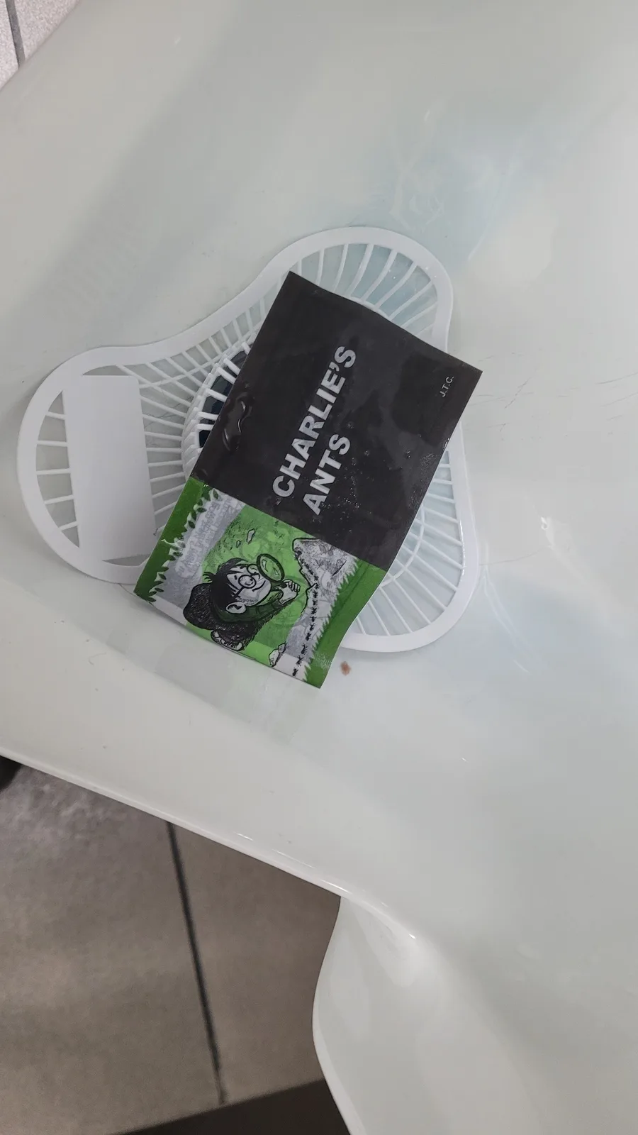 A black and green packet labeled 'CHARLIE'S ANTS' with a cartoon illustration of a boy holding a magnifying glass over an…