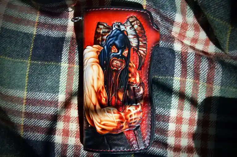 A custom leather wallet with a detailed, hand-painted design of a demonic figure with ram horns, glowing red eyes, and a…