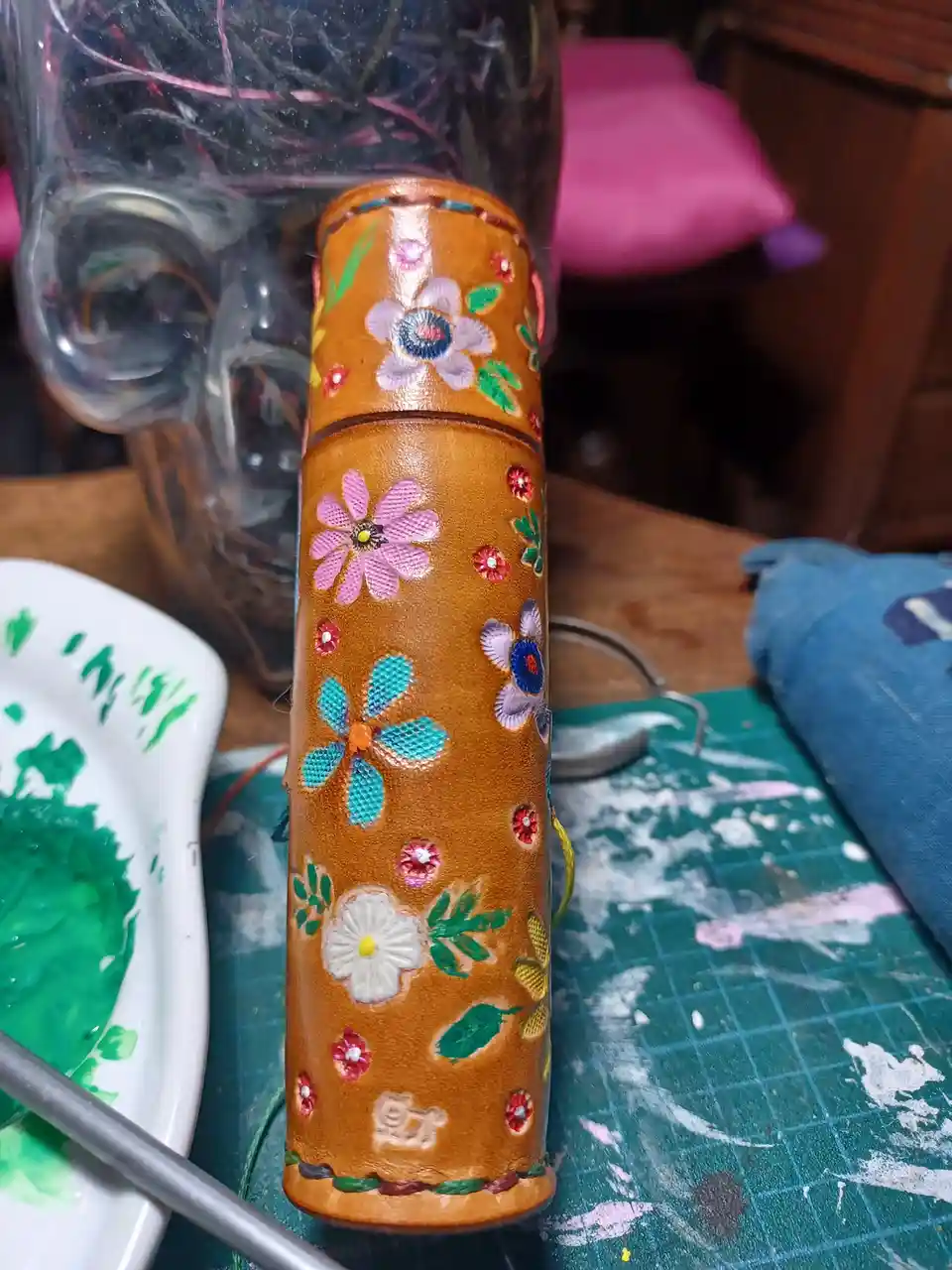 A close-up photo shows a handcrafted, cylindrical brown leather object decorated with colorful embroidered flowers and green…