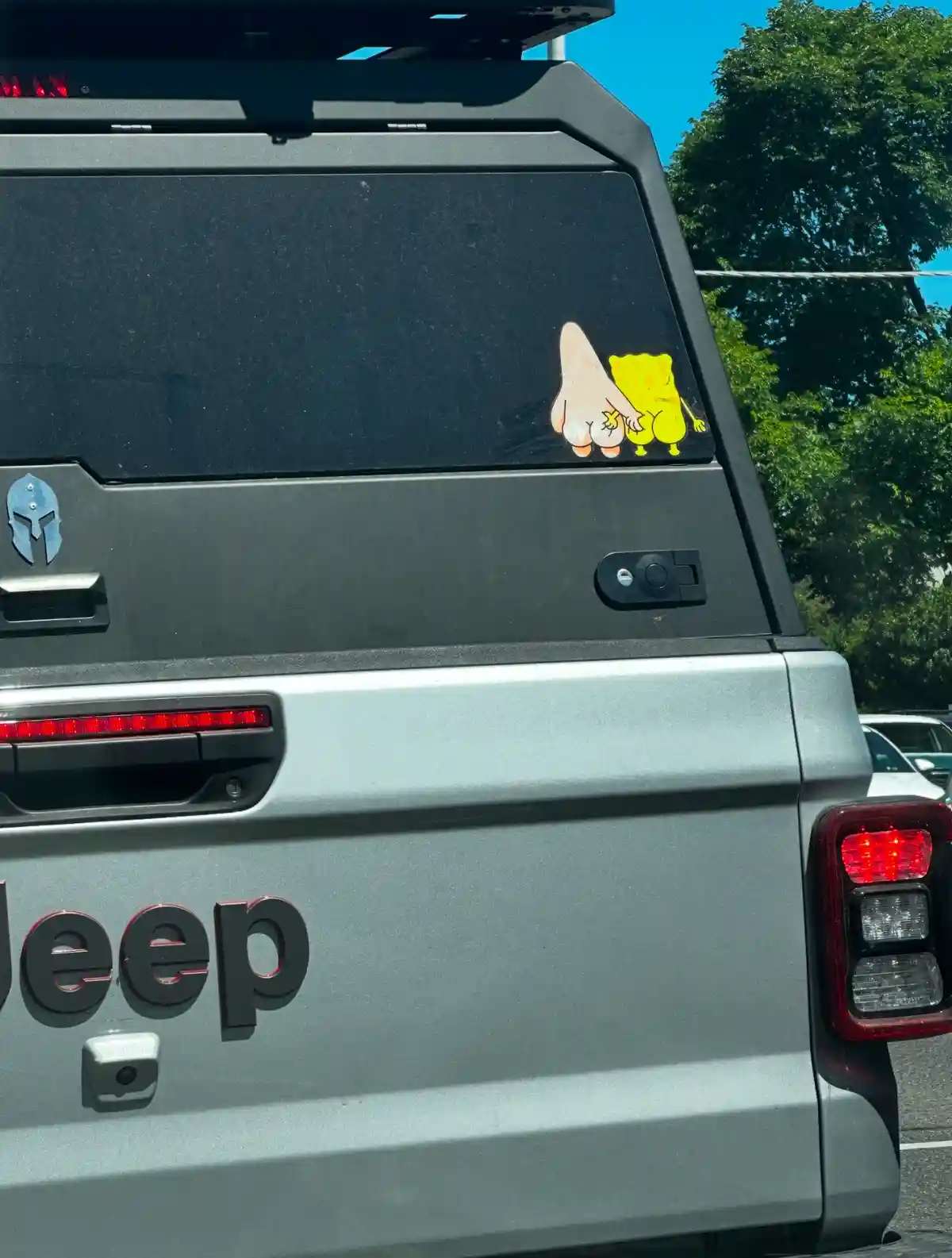 The rear of a silver Jeep SUV shows a cartoon sticker of SpongeBob SquarePants and Patrick Star holding hands on the back…