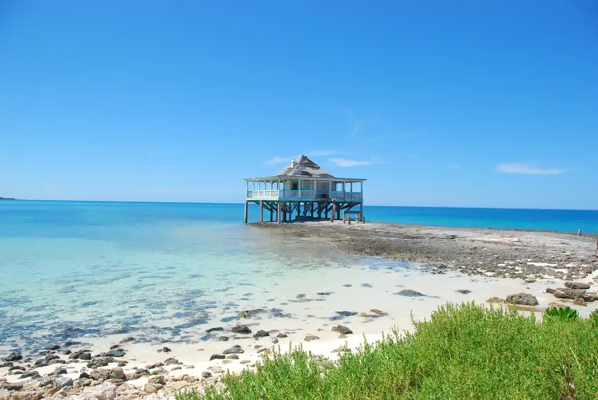 A serene tropical beach scene with clear turquoise water, white sand, and green vegetation in the foreground. A small…