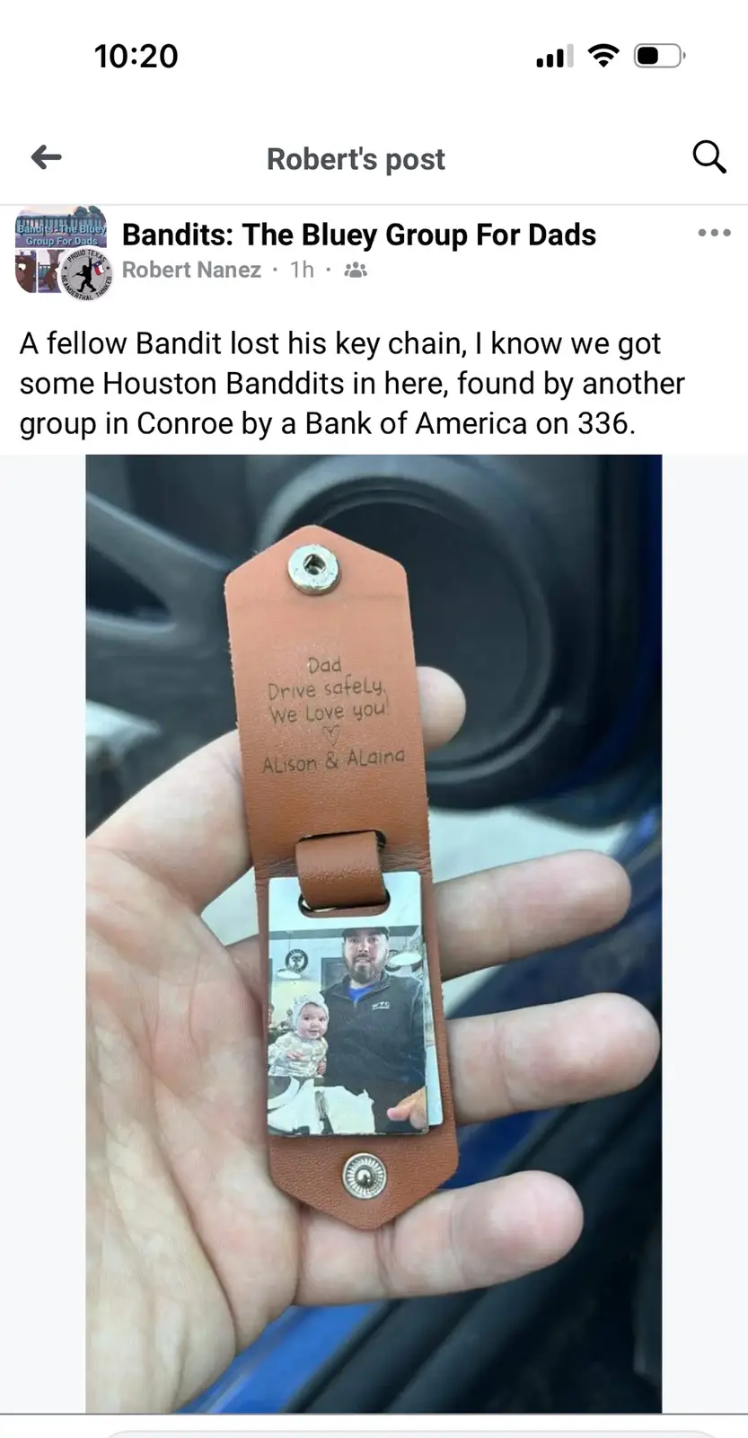 A hand holds a brown leather keychain with a photo of a man holding a baby and engraved text reading 'Dad Drive safely. We…