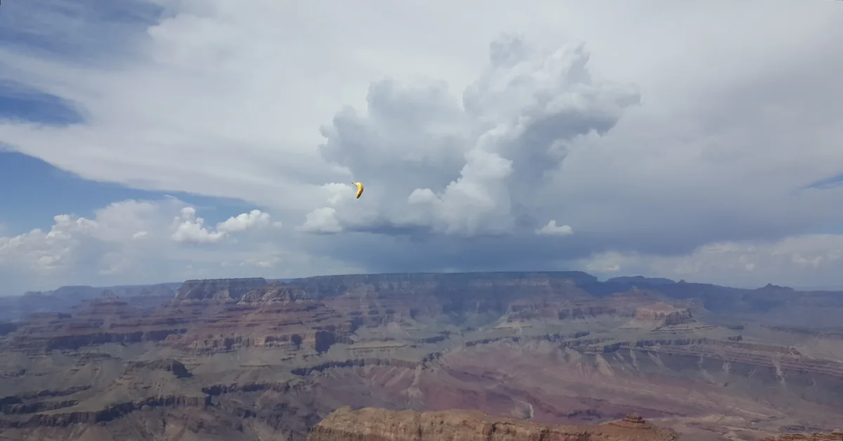 A wide-angle photograph of the Grand Canyon under a partly cloudy sky, featuring a yellow banana-shaped object floating in…