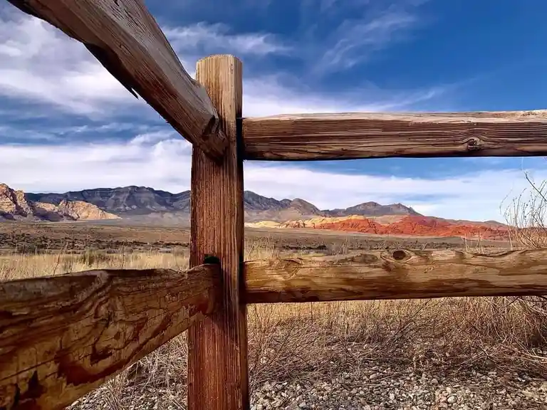 A rustic wooden fence in the foreground frames a scenic desert landscape with colorful red rock formations and distant…